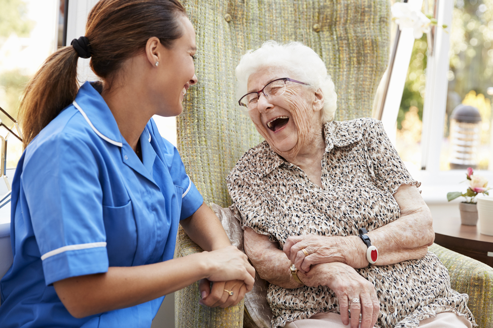 Elderly woman in chair laughing with female nurse